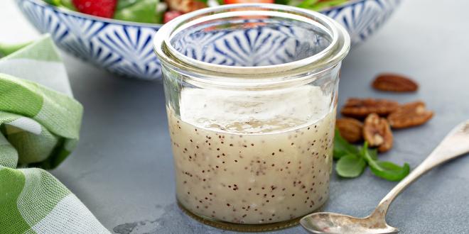 a jar of poppy seed dressing in front of a strawberry salad